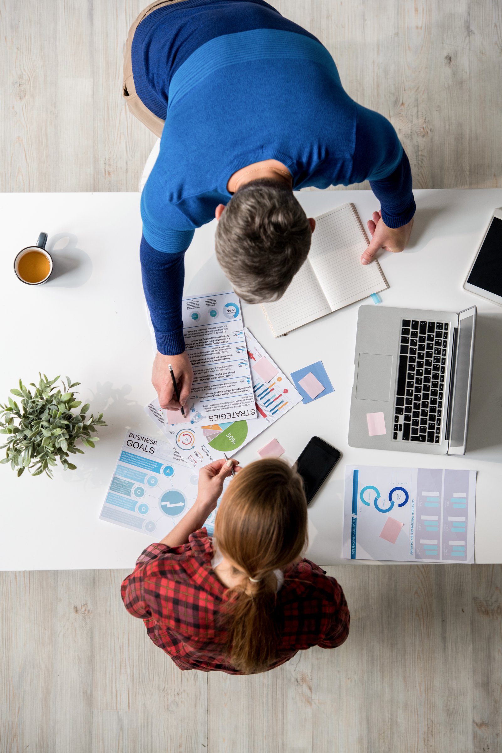 High angle view of busy young specialist in casual clothing choosing marketing strategies at meeting in office: unrecognizable man making notes on sticker while talking to colleague about plan